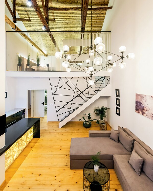 A spacious living area with a wooden floor, a modern staircase, a sofa, and a dining area with a black countertop.