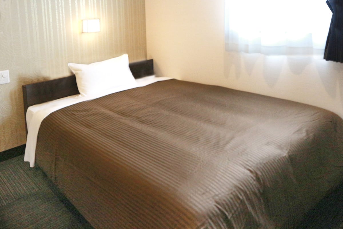 Ein Hotelzimmer mit einem großen Bett, einem Kopfteil, einer Wandleuchte und einem fenster mit Vorhängen.