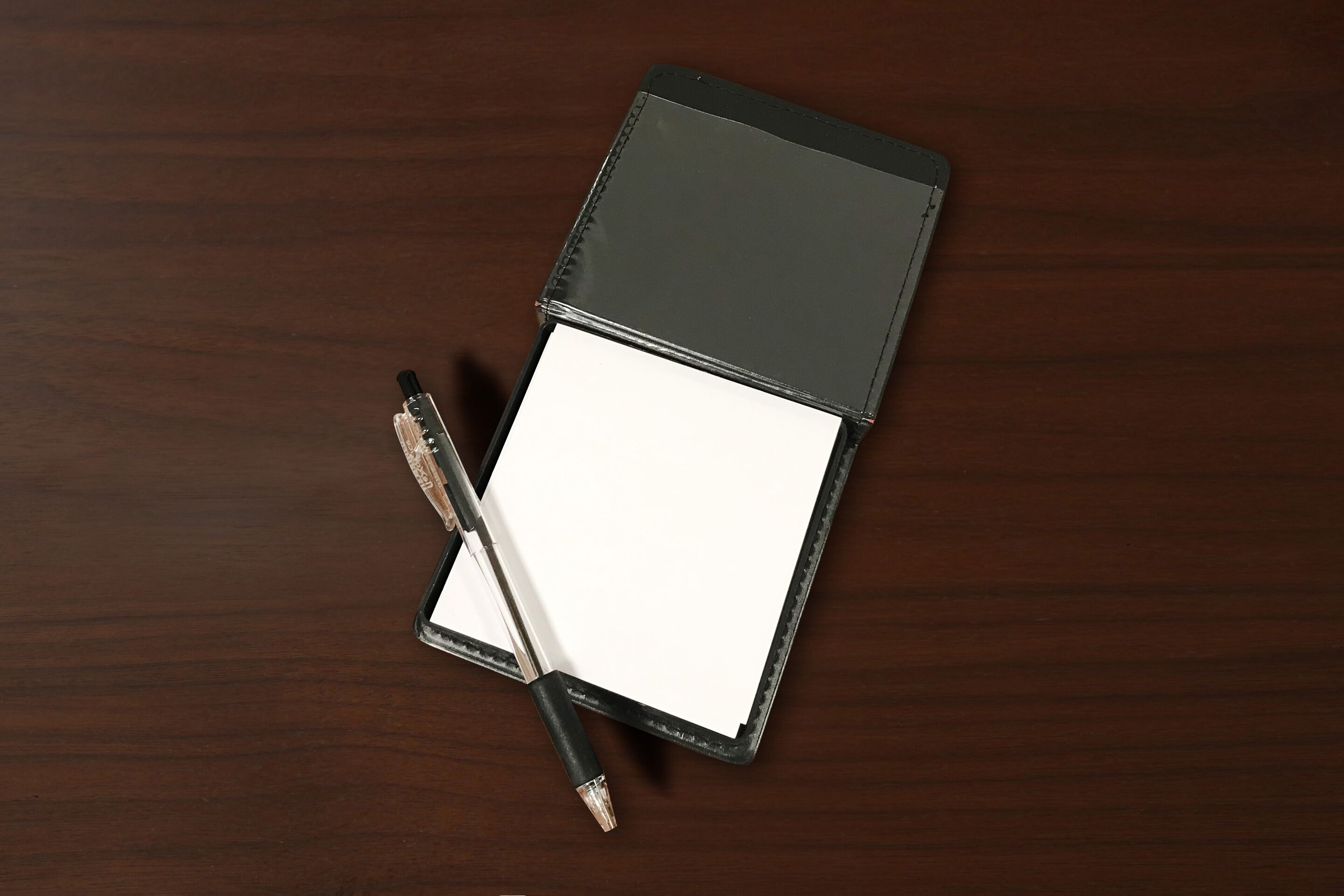 A closed notebook with a pen on a wooden surface.