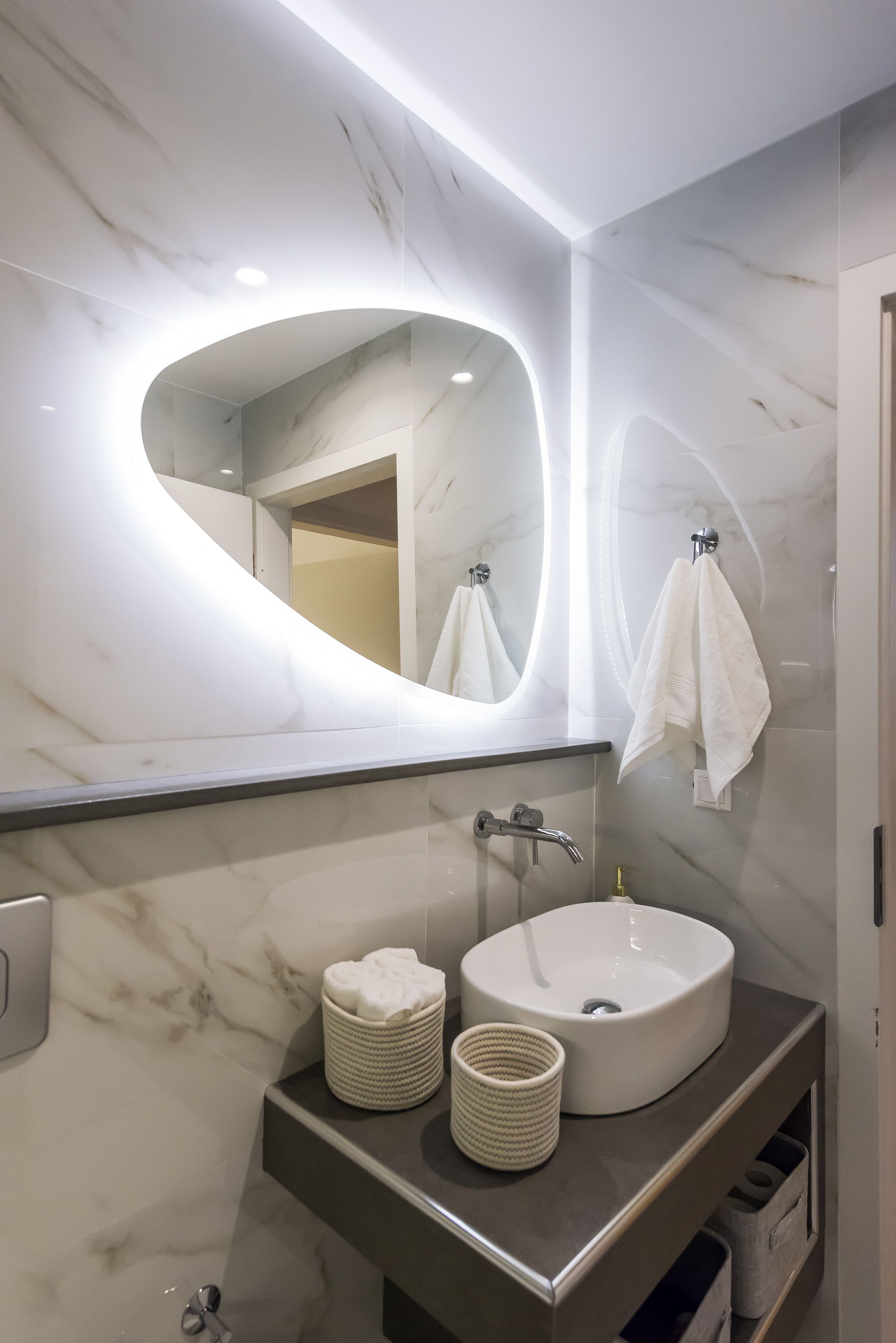 A modern bathroom with a marble vanity, a large oval mirror, and a round sink.