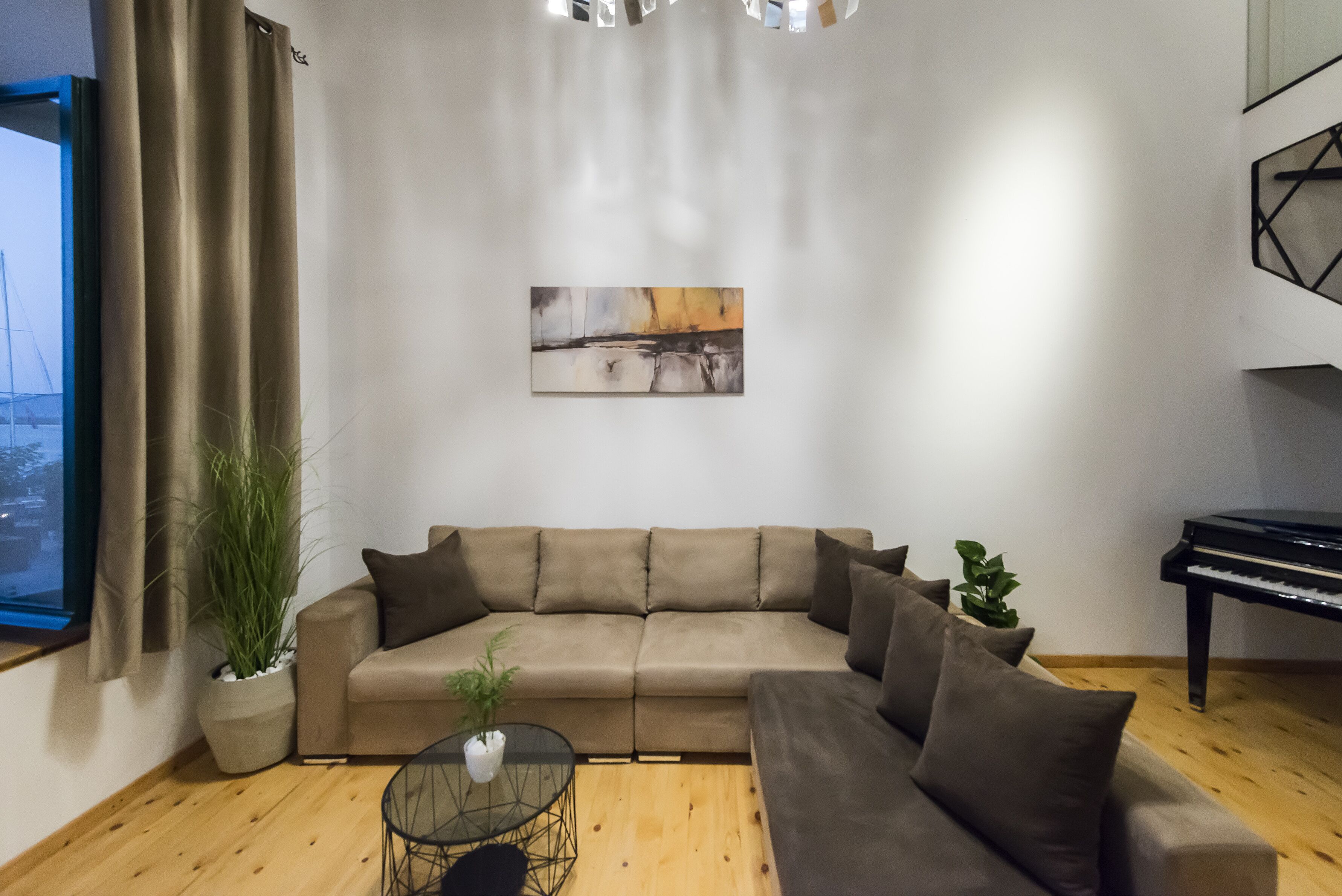 En stue med en beige hjørnesofa, et glasbord og et klaver.