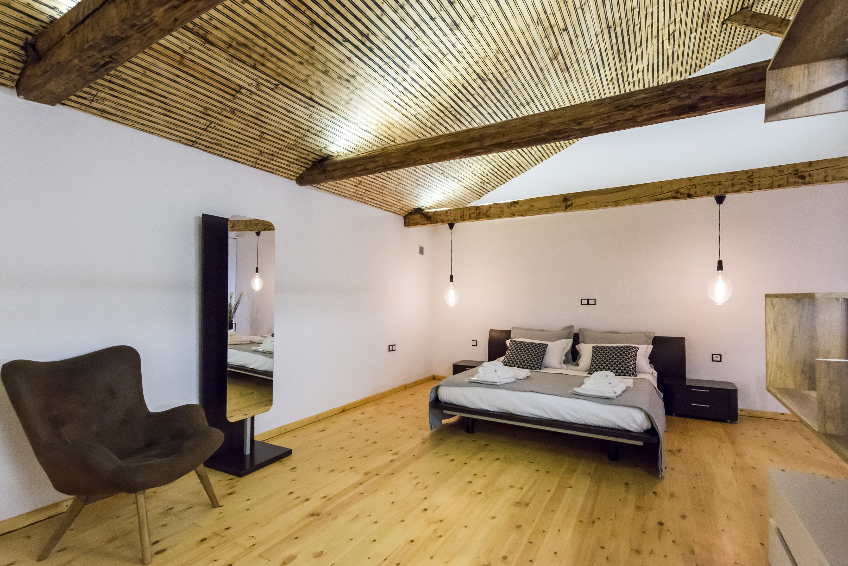 Un dormitorio con techo de madera, una cama con almohadas, una silla y un espejo.