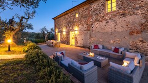 A stone building with a patio area featuring wicker furniture and a table, illuminated by outdoor lighting.