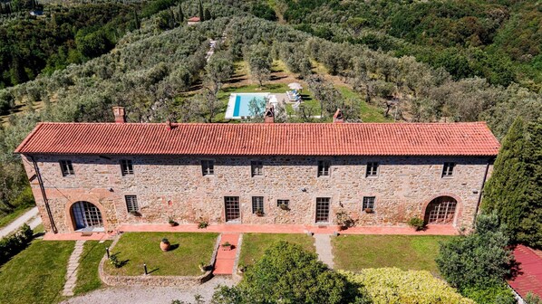 A stone building with a red-tiled roof, a swimming pool, and a well-maintained garden.