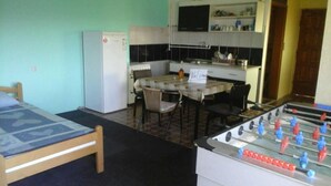 Una habitación con cama, mesa de comedor con sillas, cocina con televisor y mesa de futbolín.