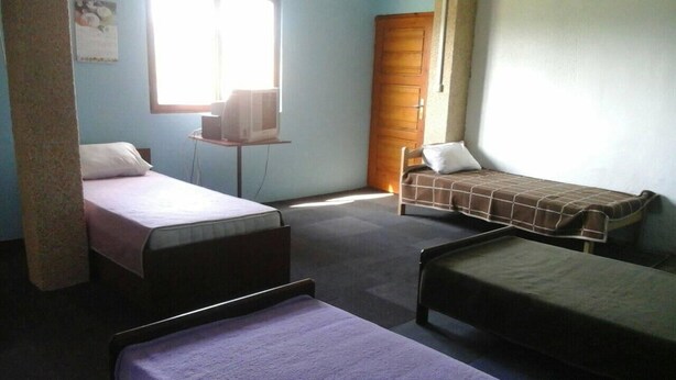 Habitación tipo dormitorio con dos camas individuales, un escritorio pequeño con una computadora y una ventana que proporciona luz natural.