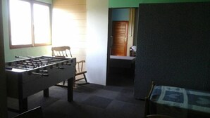 Una habitación con una mesa de fútbol de mesa, un sillón mecedora y una puerta que da a otra habitación.