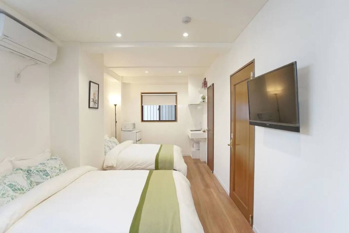 A hotel room with two beds, a TV, a bathroom, and a hallway leading to another room.