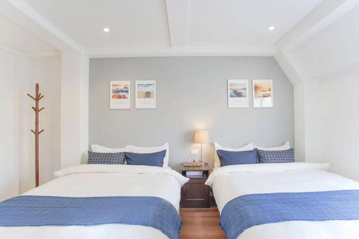 A double room with two beds, a coat rack, a nightstand with a lamp, and framed pictures on the wall.