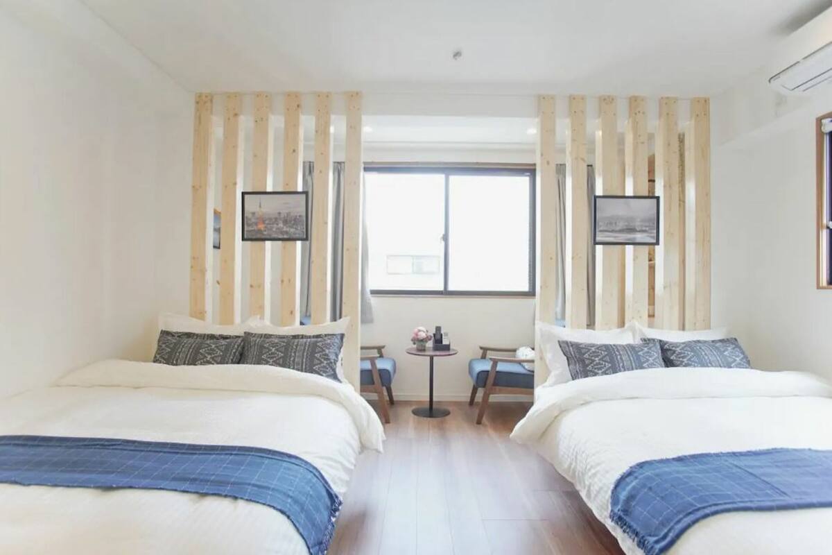 A hotel room with two beds, a small table with chairs, and a window with curtains.