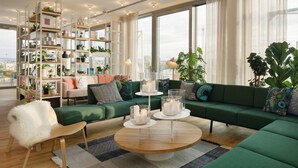 A modern living room with a green sofa, a wooden coffee table, and a glass shelving unit filled with plants and decorative items. - Zoku Vienna (Vienna)