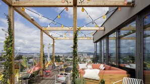 A rooftop terrace with a wooden pergola, string lights, seating area, and a view of the cityscape. - Zoku Vienna (Vienna)