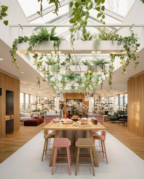 Un interior moderno con zona de comedor central, suelo de madera y plantas colgantes.