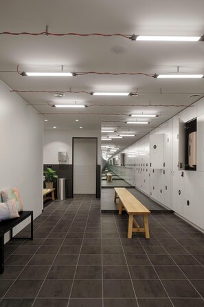 A modern office space with a long corridor, lockers, a bench, and a trash bin.