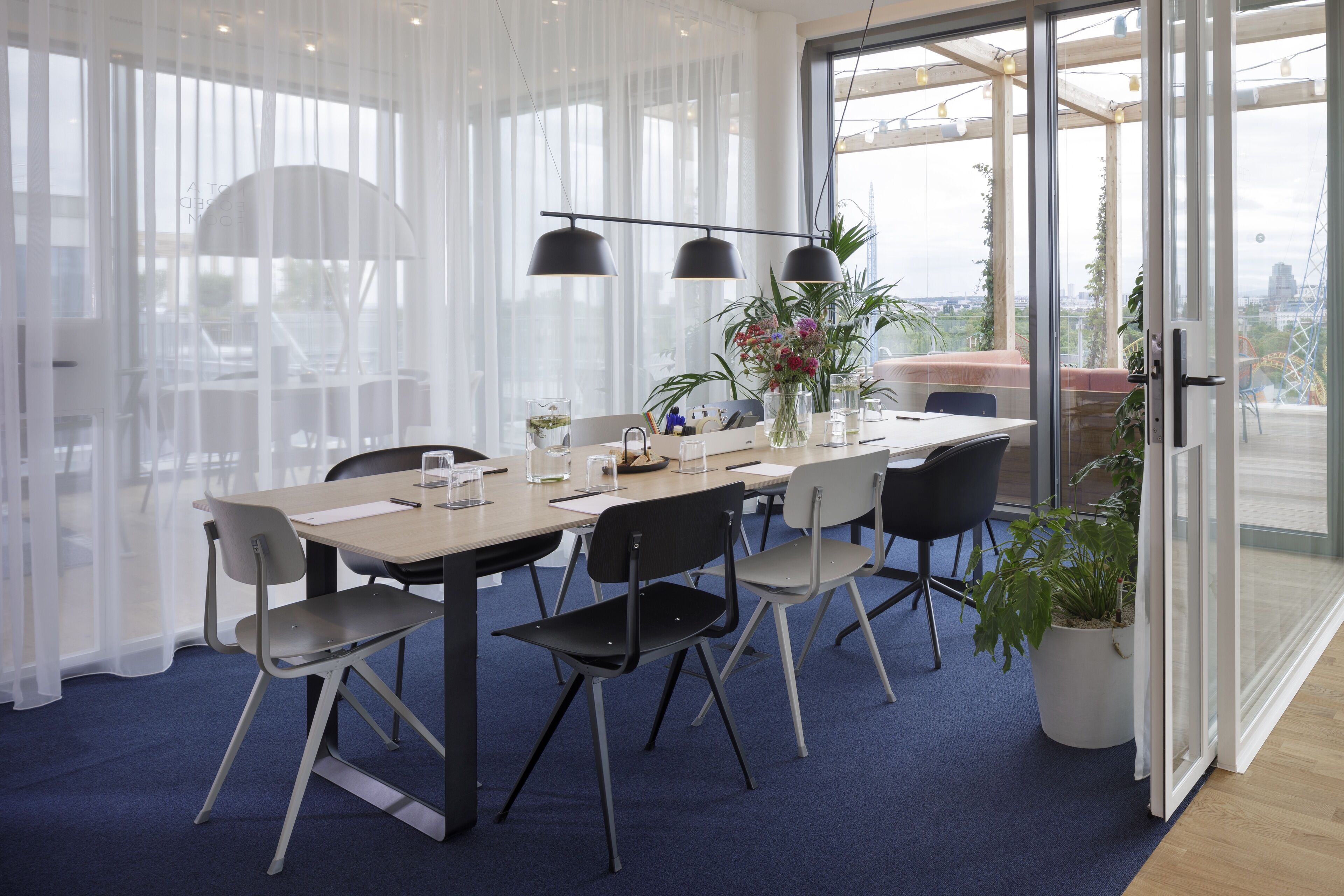 A modern dining area with a long table, chairs, and pendant lighting.