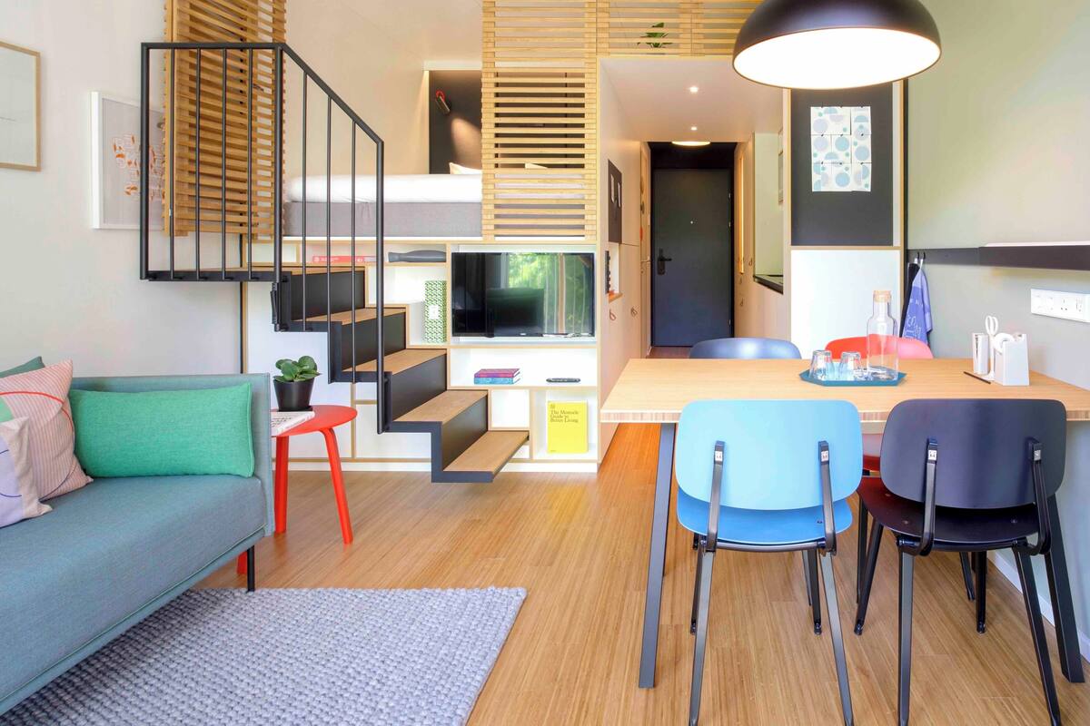 Un interior moderno con sofá, mesa de comedor, sillas, televisor y una escalera.