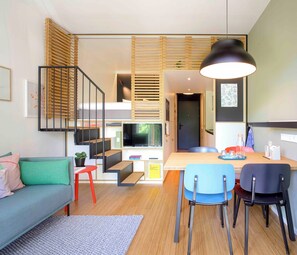 A modern interior with a sofa, dining table, chairs, a TV, and a staircase.