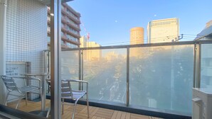 A balcony with a view of a cityscape, including a tall building and a crane. There are metal chairs and a table on the balcony. - Pangoo Shinagawa (Tokyo)