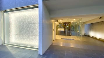 A modern building entrance with a glass door, tiled walls, and a tiled floor.
