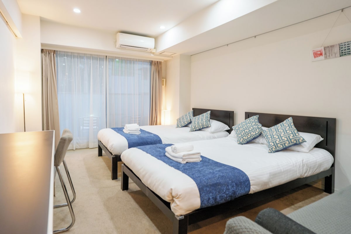 Quarto de hotel com duas camas, uma escrivaninha e uma janela com cortinas.