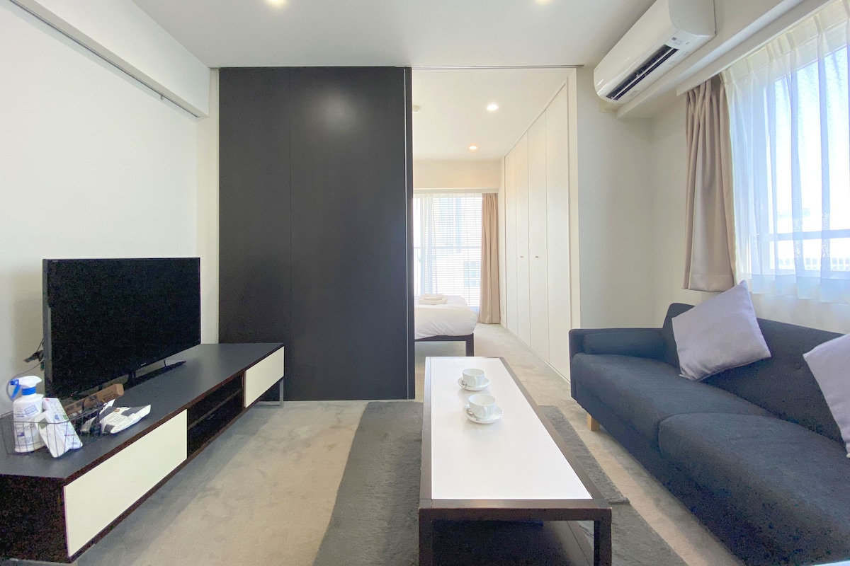 Uma sala de estar moderna com televisão de tela plana, um sofá, uma mesa de centro e uma janela grande com cortinas.