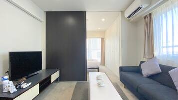 Uma sala de estar moderna com televisão de tela plana, um sofá, uma mesa de centro e uma janela grande com cortinas.