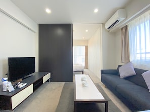 Uma sala de estar moderna com televisão de tela plana, um sofá, uma mesa de centro e uma janela grande com cortinas.