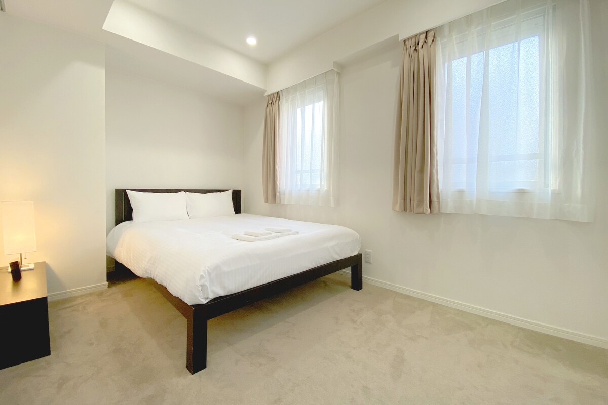 Quarto com cama, mesa de cabeceira e janela com cortinas.