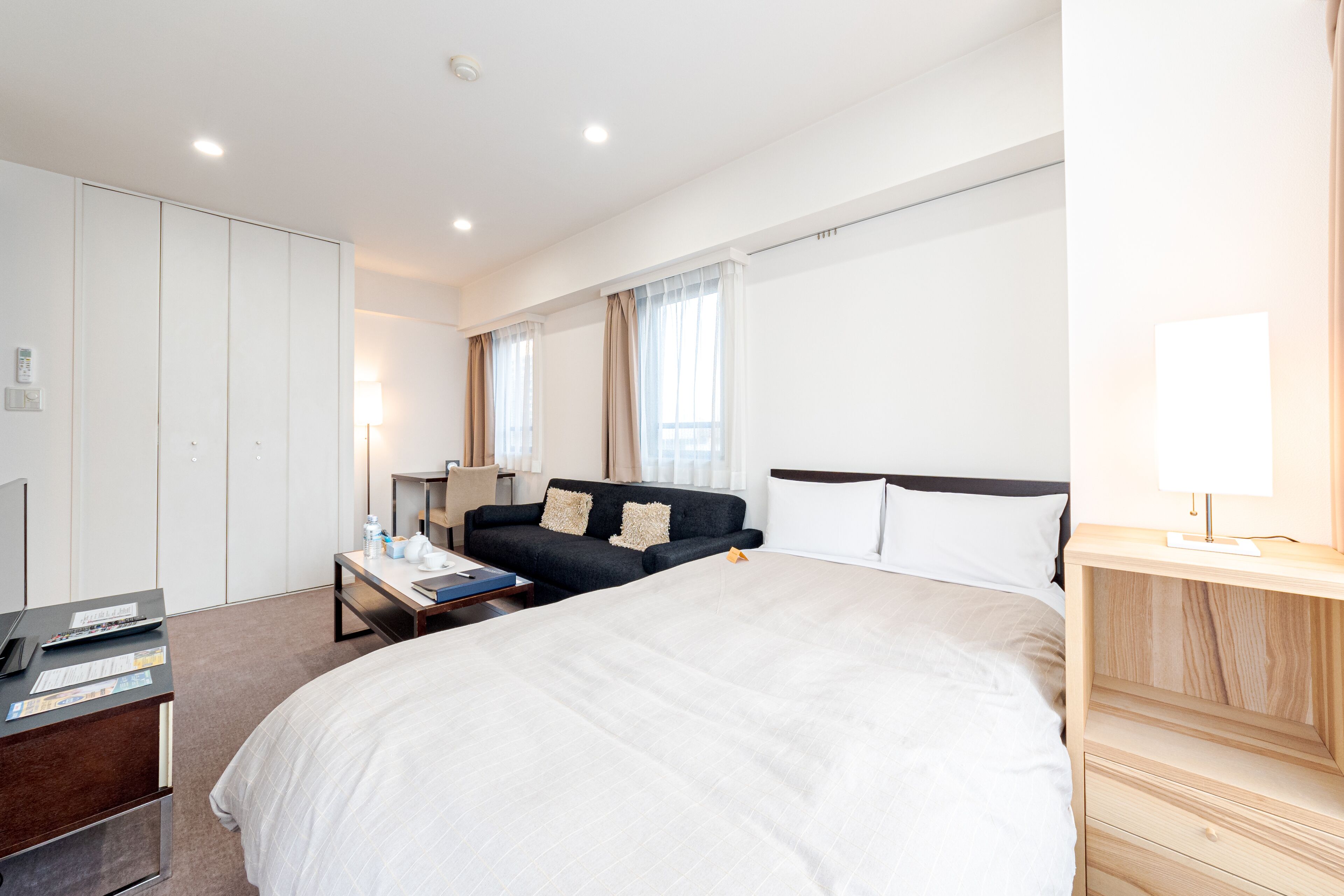 A hotel room with a large bed, a desk with a laptop, a sofa, and a wardrobe.