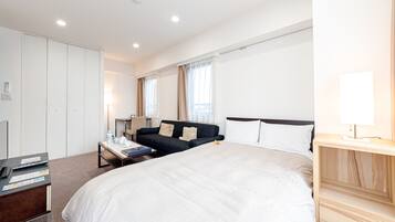 A hotel room with a large bed, a desk with a laptop, a sofa, and a wardrobe.