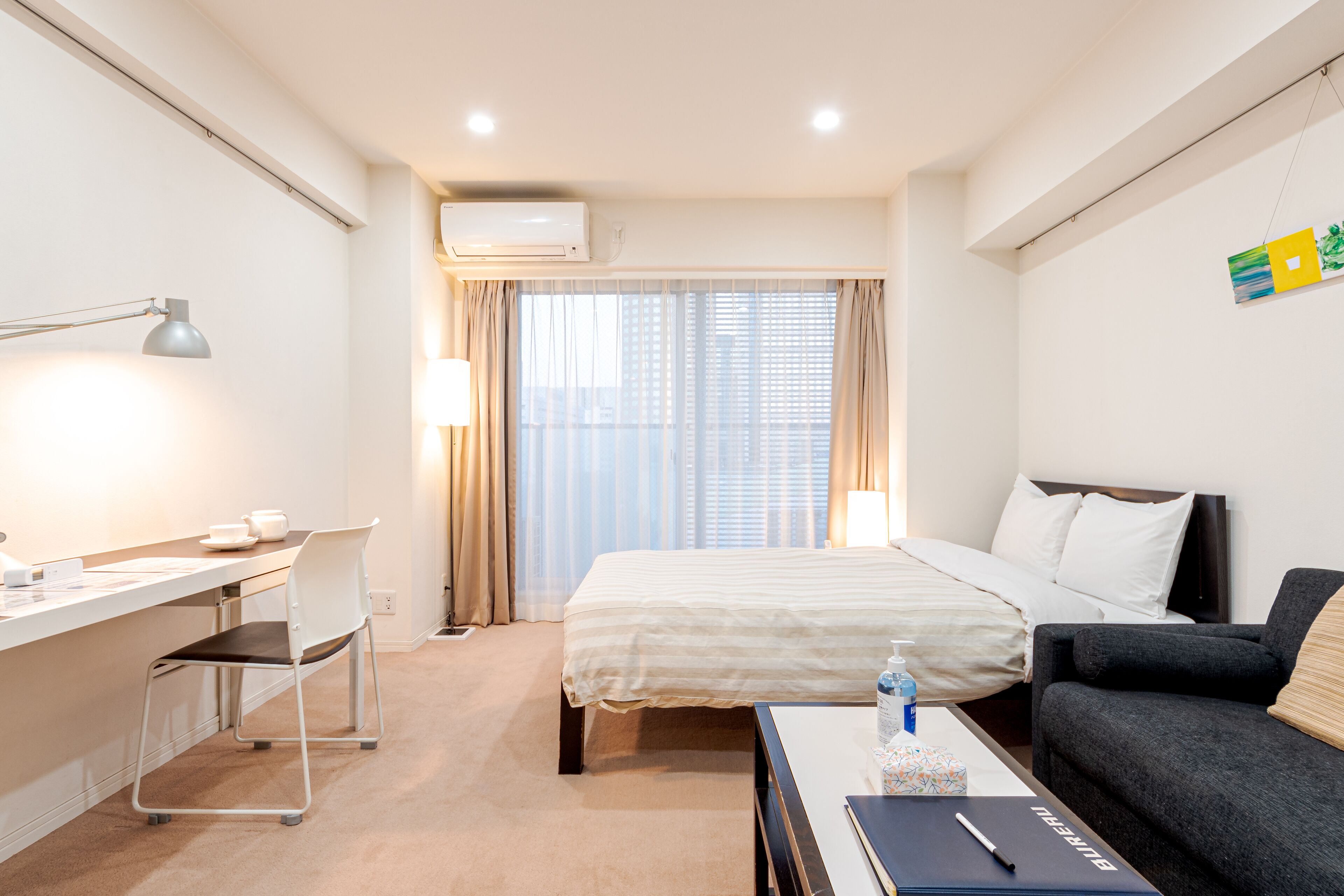 Una habitación de hotel con una cama, un escritorio con una silla, un sofá y un ventanal con cortinas.