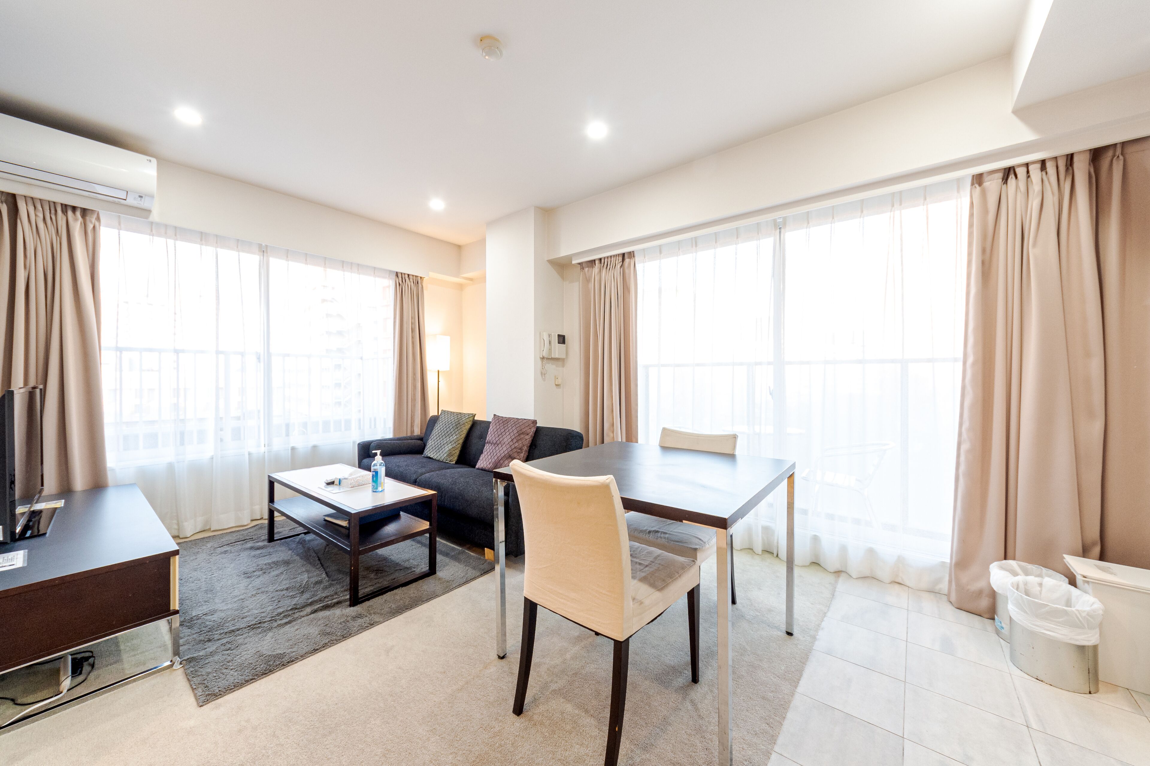 A modern hotel room with a sofa, dining table, and TV.