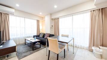 A modern hotel room with a sofa, dining table, and TV.