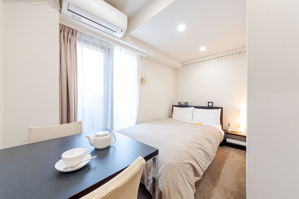 Quarto de hotel com cama, mesa de cabeceira e janela com cortinas.