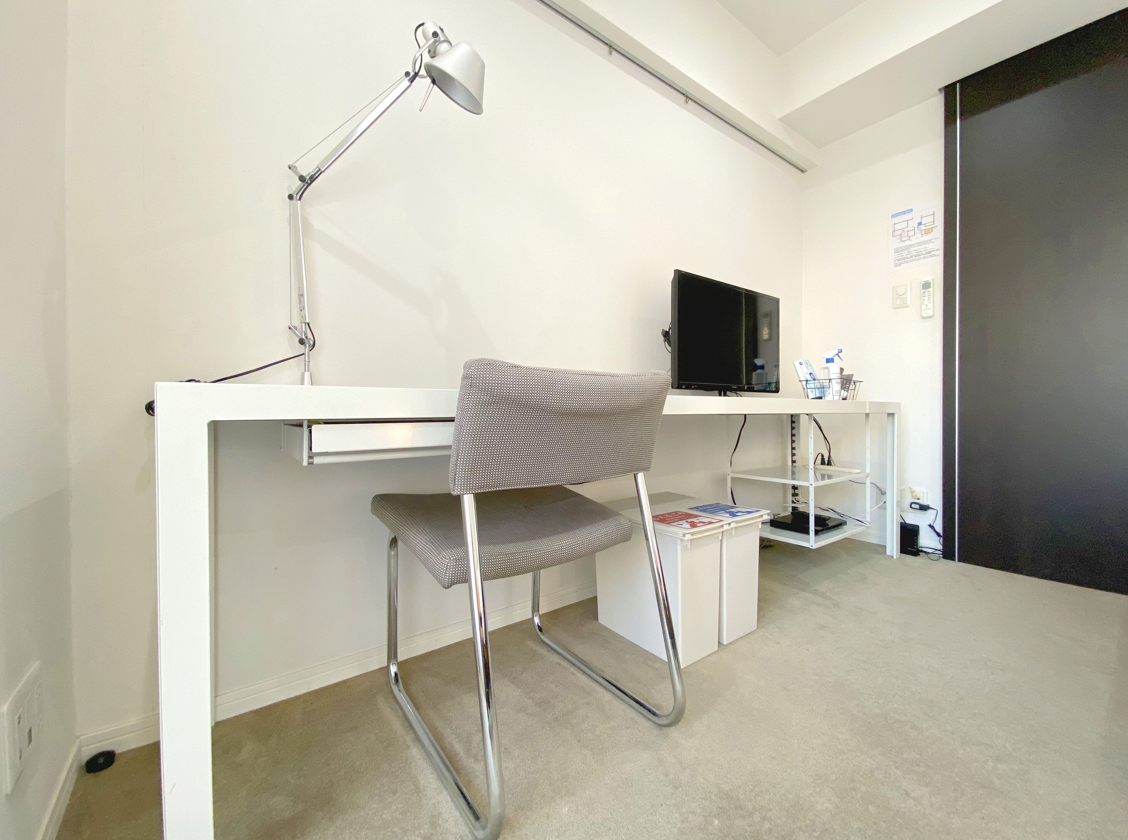 Un espacio de trabajo pequeño y moderno, con escritorio, silla, monitor de computadora y lámpara.