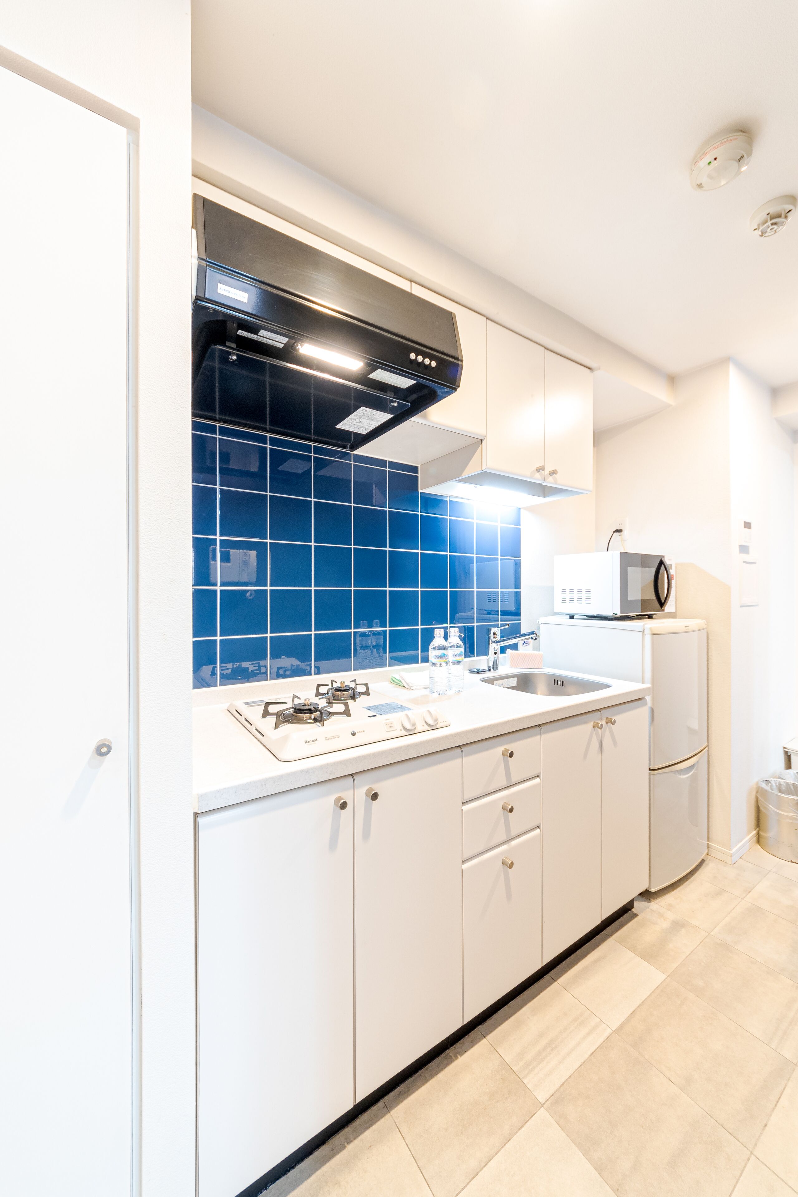 A modern kitchen with white cabinets, a blue backsplash, a gas stove, a microwave, and a sink.