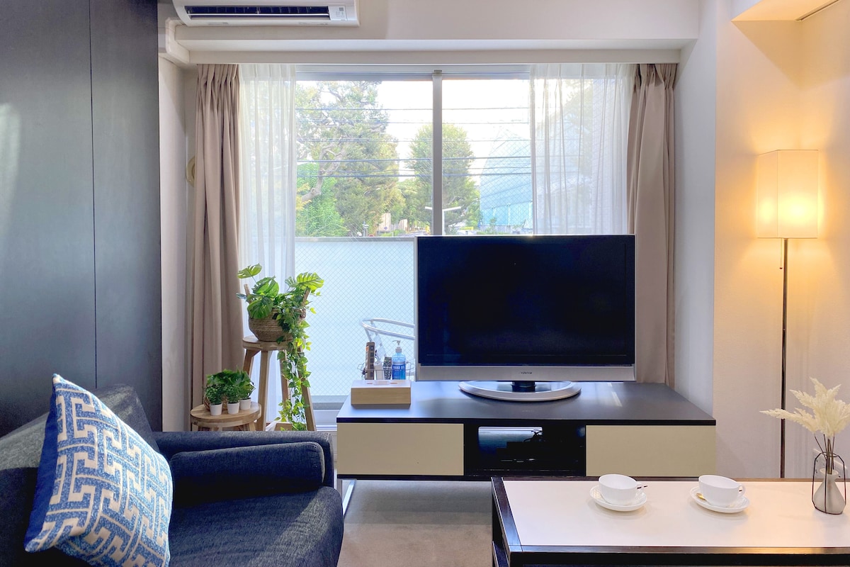 Uma sala de estar moderna com uma televisão de tela plana, um sofá, uma mesa de centro com xícaras e um vaso de planta.