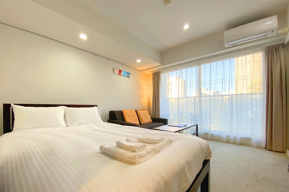 Quarto de hotel com uma cama grande, um sofá, uma mesinha e uma janela com cortinas.