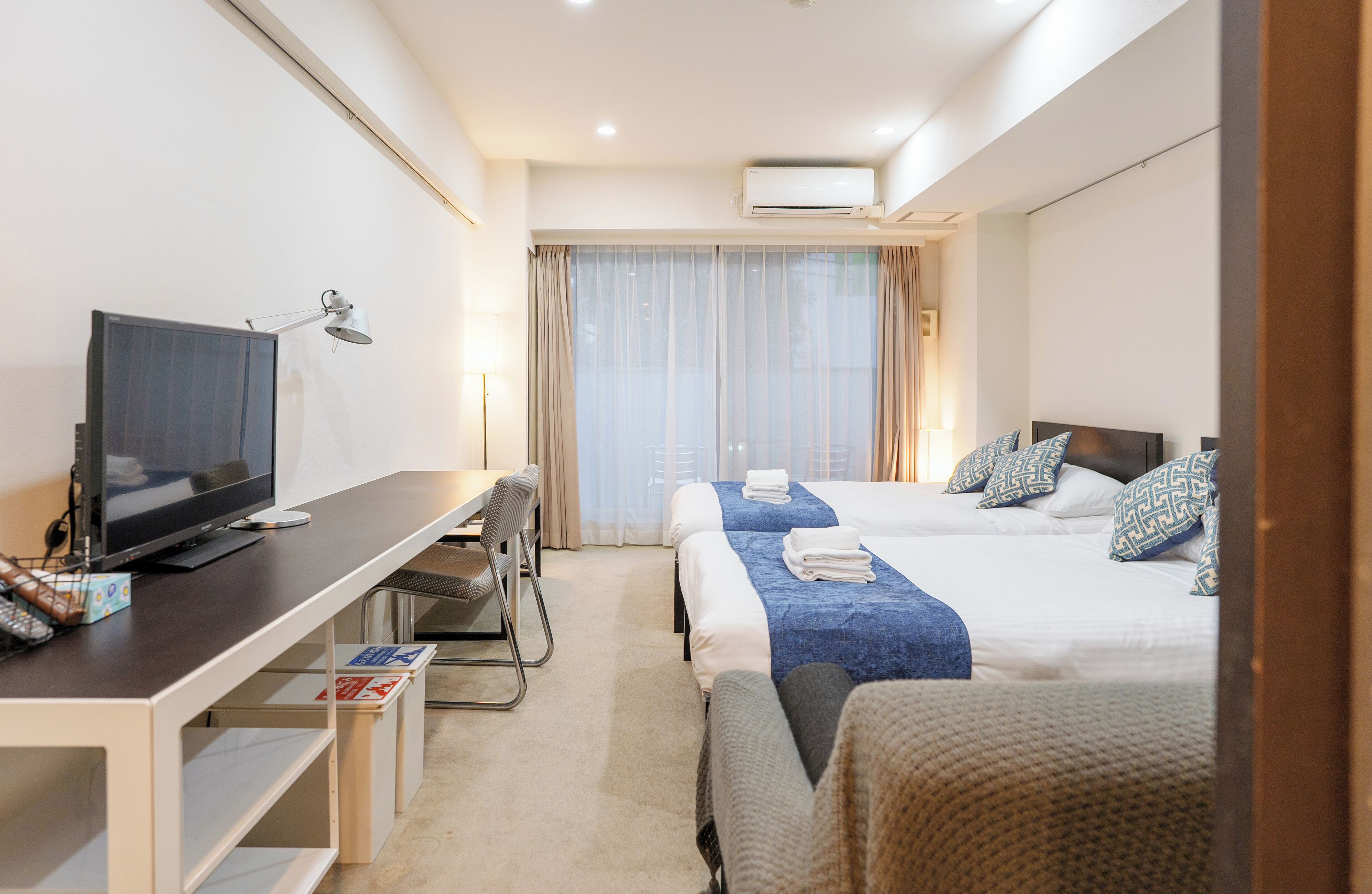 A hotel room with a bed, a desk with a television, a chair, and a window with curtains.