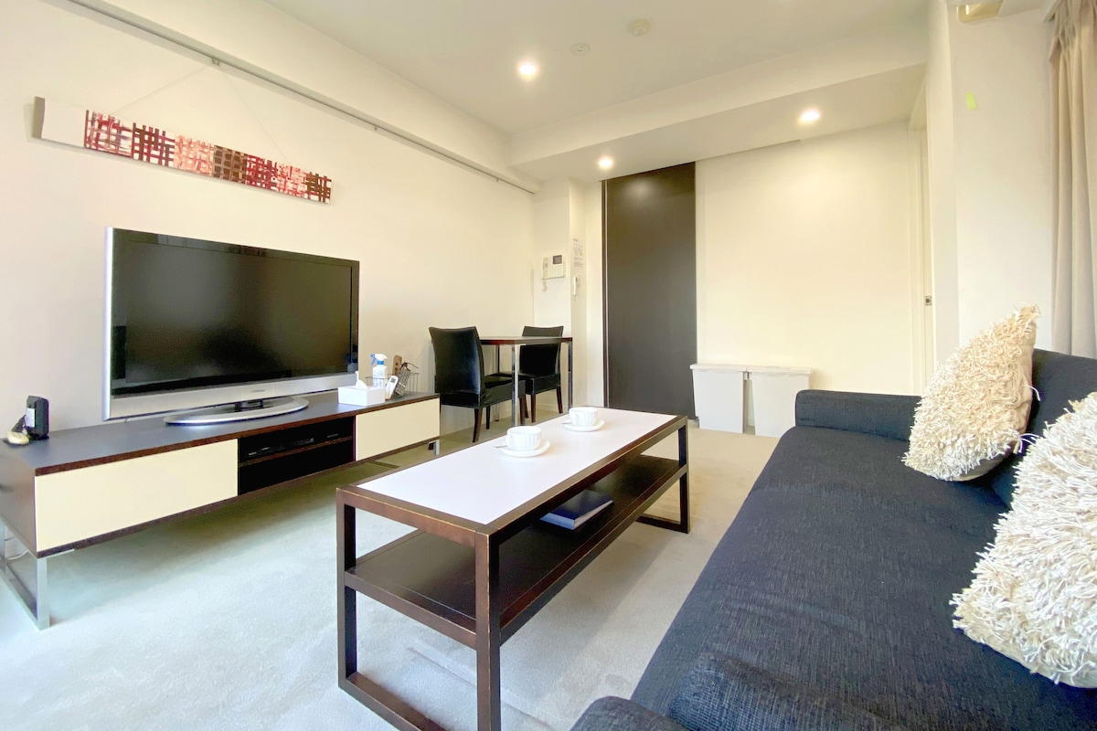 Uma sala de estar moderna com televisão de tela plana, mesa de centro, sofá e área de jantar com cadeiras.