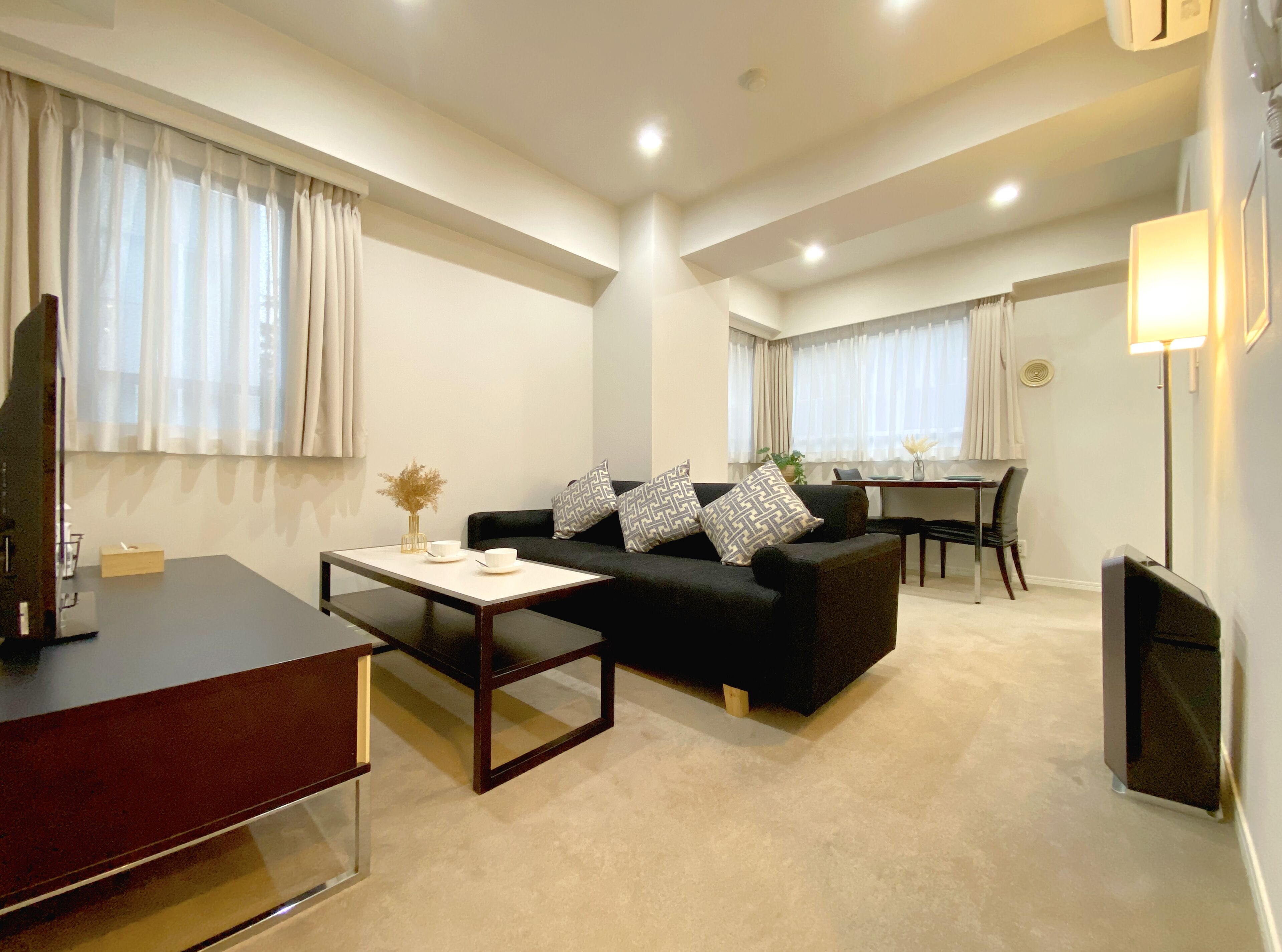 A modern living room with a black sofa, a coffee table, and a dining area in the background.