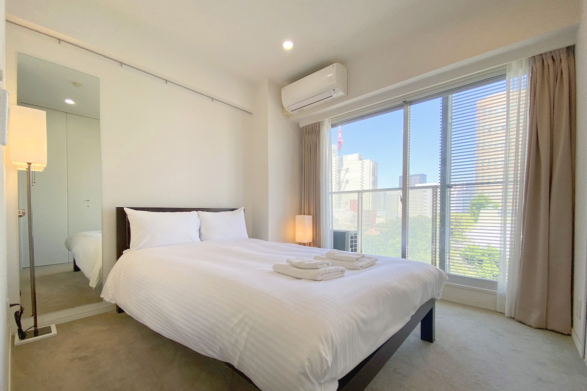 Quarto de hotel com uma cama grande, ar condicionado, luminária de cabeceira e vista para a cidade pela janela.