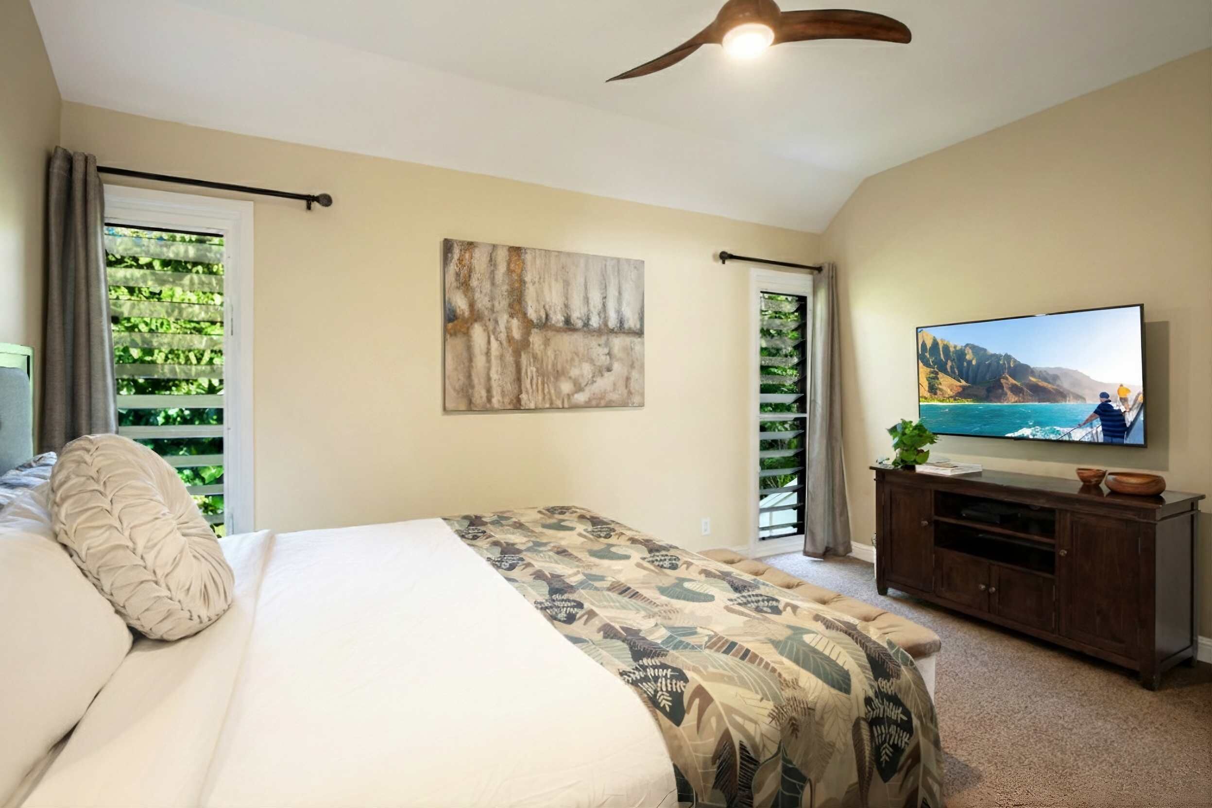 A bedroom with a bed, a ceiling fan, a TV, and a window with a view of greenery.