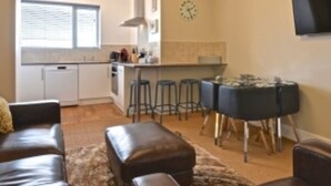 A modern living room with a leather sofa, a coffee table, and a rug. There is a kitchen area with a dining table and bar stools. - Rockcliffe Boutique 2-bed Apartment in Whitby (Whitby)