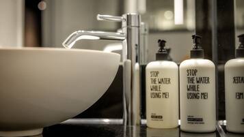 A bathroom sink with a mirror, a faucet, and three bottles of hand soap labeled "STOP THE WATER WHILE USING ME!"