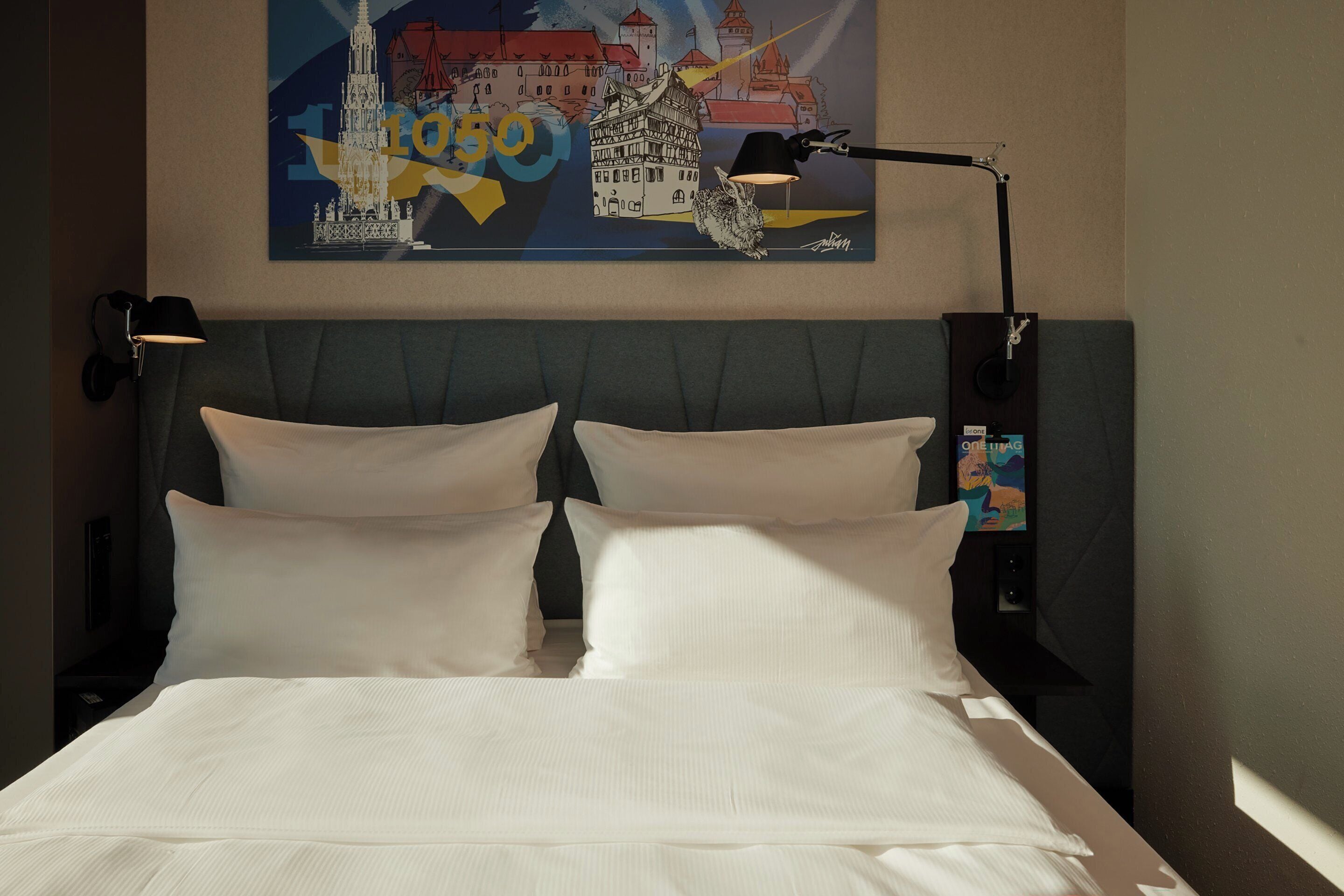 A hotel room with a bed, two bedside lamps, and a painting on the wall.