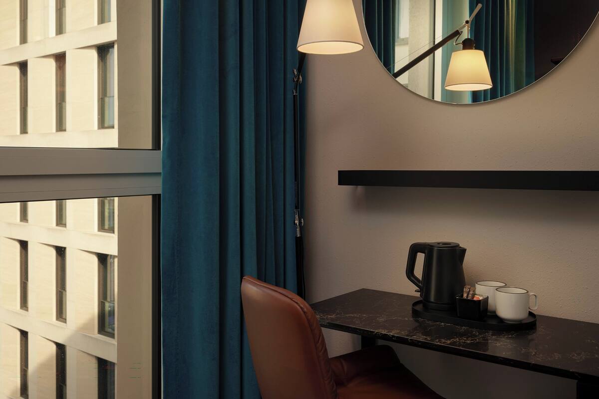 A hotel room with a desk, a coffee maker, two mugs, a chair, and a mirror on the wall.
