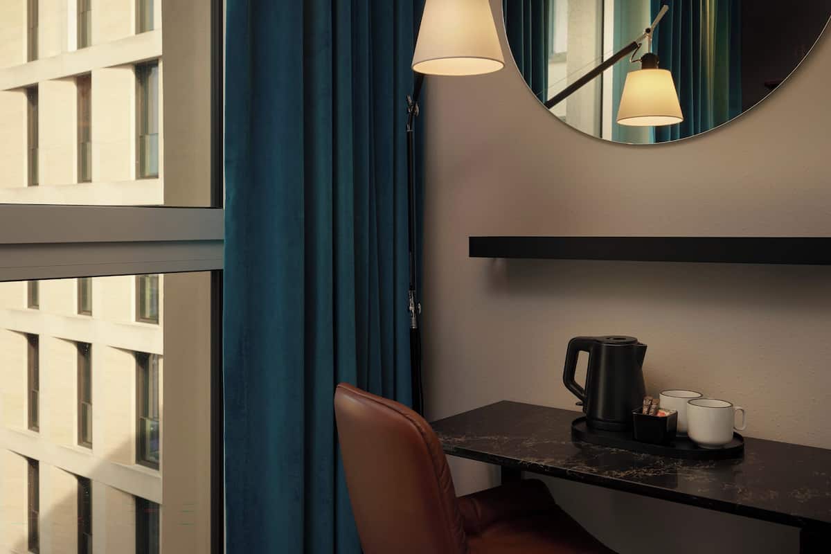 Een hotelkamer met een bureau, een koffiezetapparaat, twee mokken, een stoel en een spiegel aan de muur.