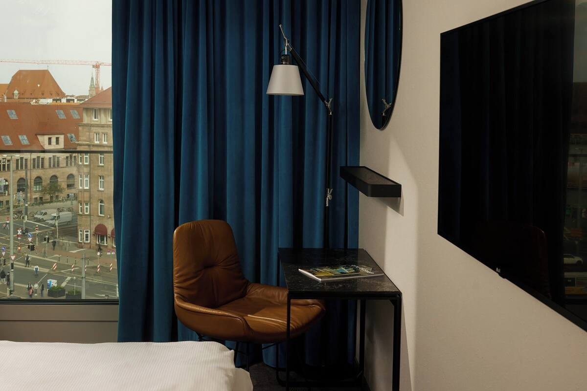 Hotelkamer met uitzicht op een stadsbeeld, een bruine leren fauteuil, een klein tafeltje met een tijdschrift en een zwarte lamp.