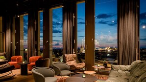A modern lounge with large windows, leather sofas, and a city view at dusk. - The Cloud One Nürnberg, by the Motel One Group (Nuremberg)